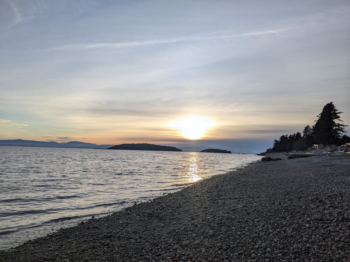 sun sets over mountains at a pebble beach on the west coast